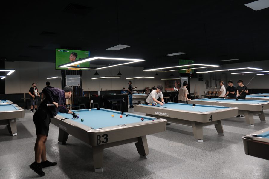 Wide view of Kirkwood Billiards floor with pool tables, players in action, and World Cup on the TVs